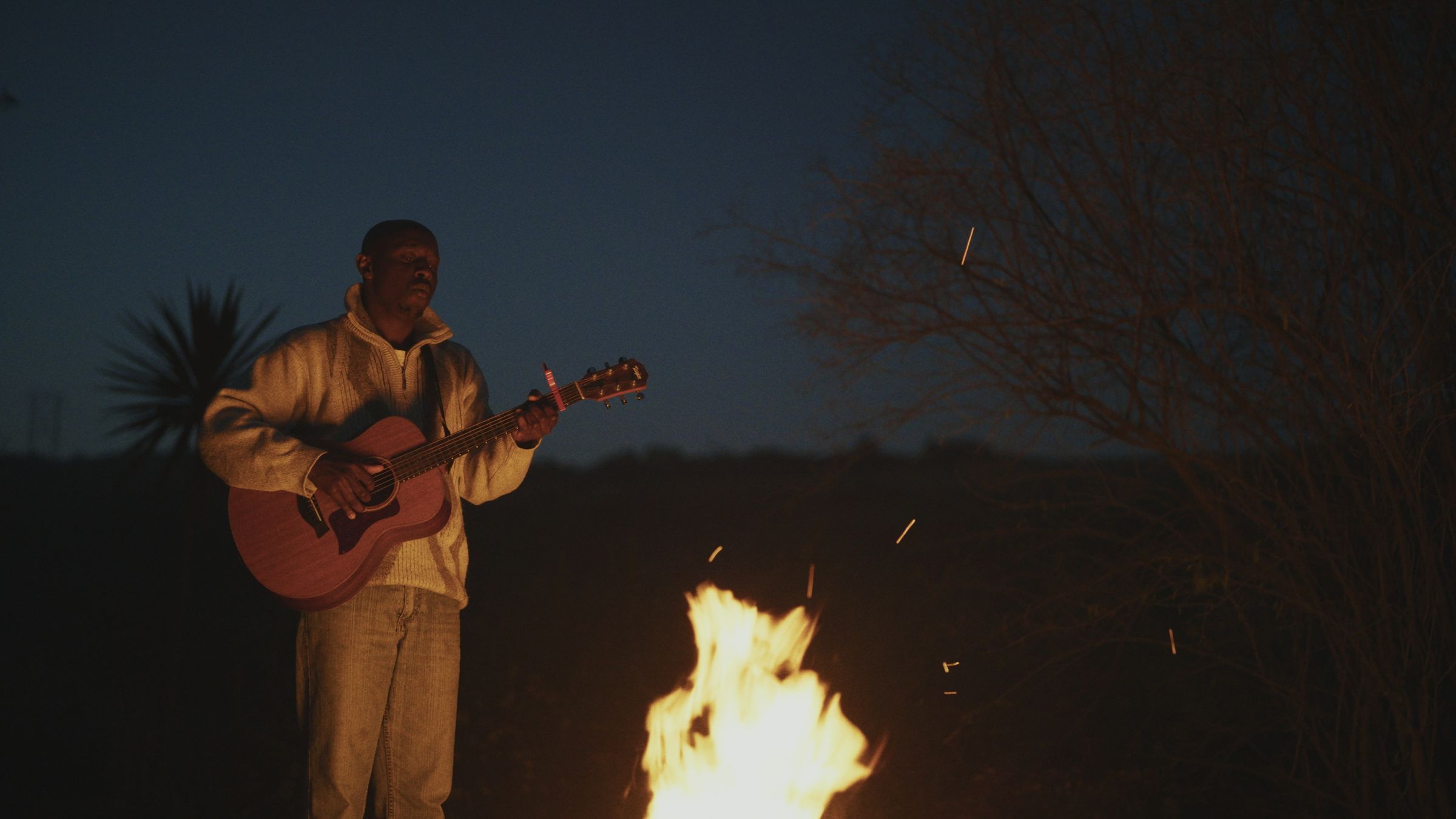 Jabulile Majola playing guitar beside a fire at dusk